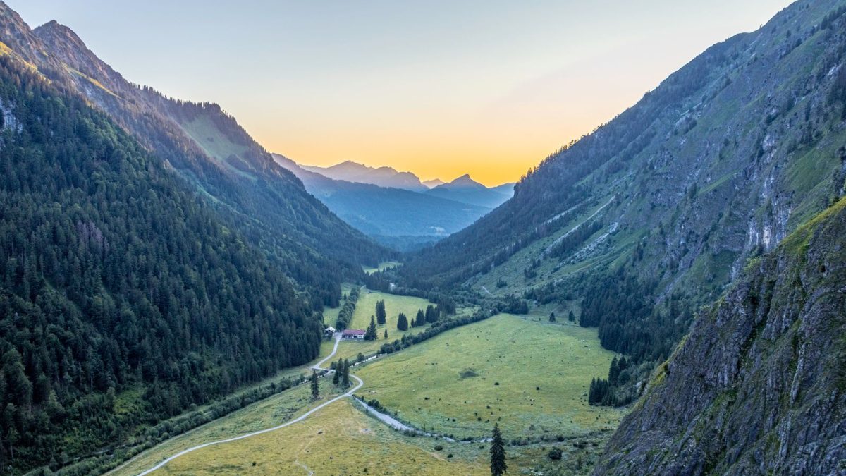 Alpine valley with a green meadow between steep mountain slopes at sunrise
