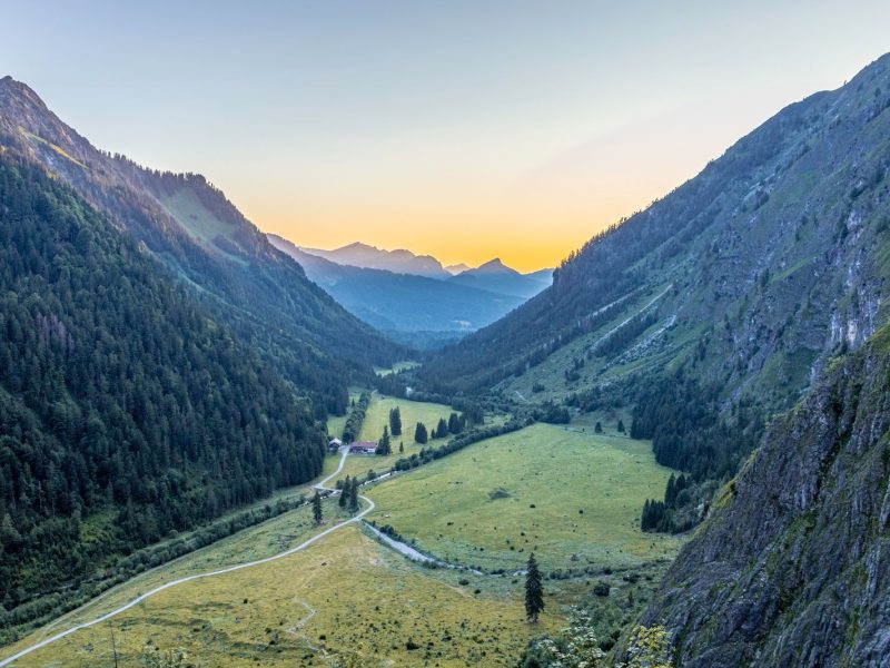 Alpine valley with a green meadow between steep mountain slopes at sunrise