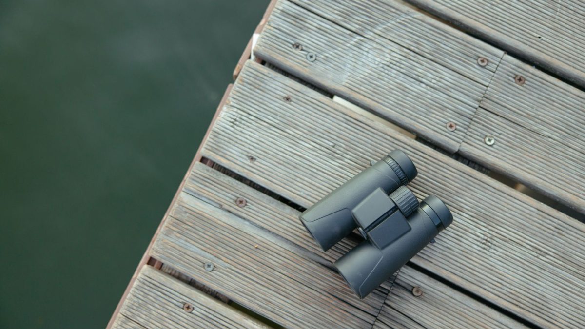 Compact binoculars resting on a weathered wooden dock beside a lake