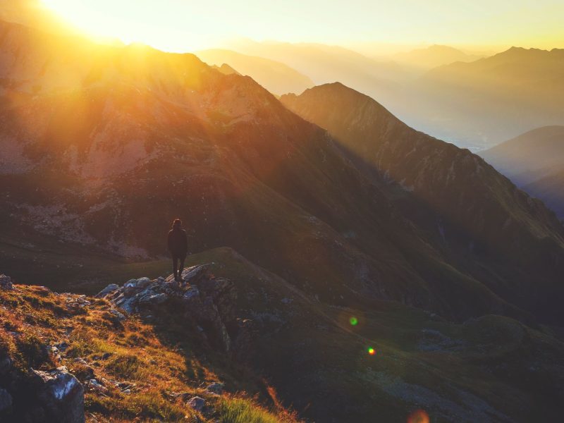 Lone hiker standing on a rocky mountain ridge in golden light