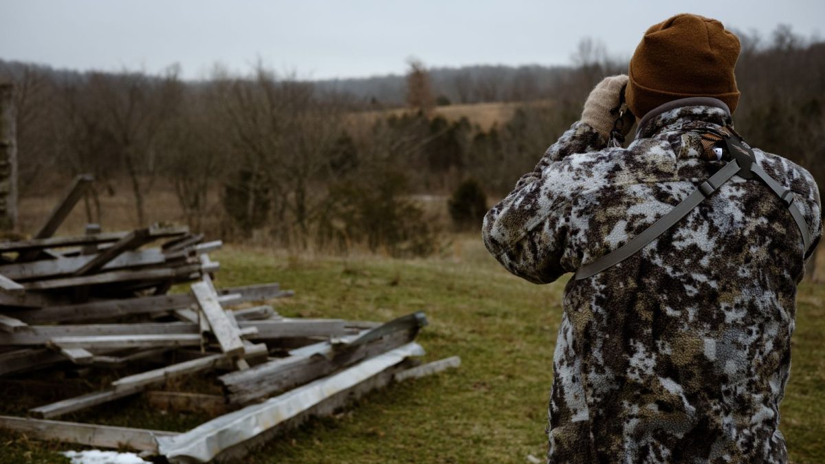 Hunter in camouflage raising binoculars to scan a field edge