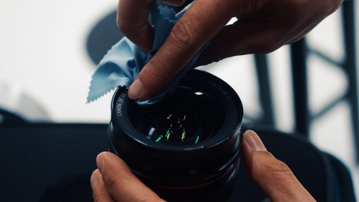 Hands cleaning an optical lens with a microfiber cloth