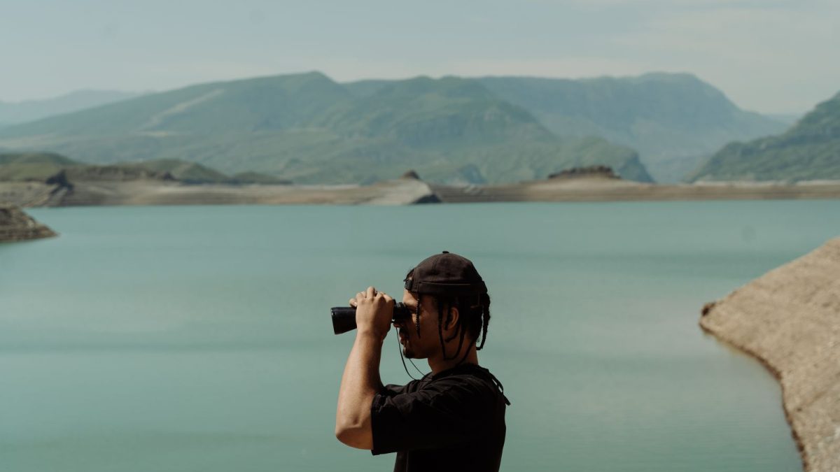 Man using binoculars beside a mountain lake