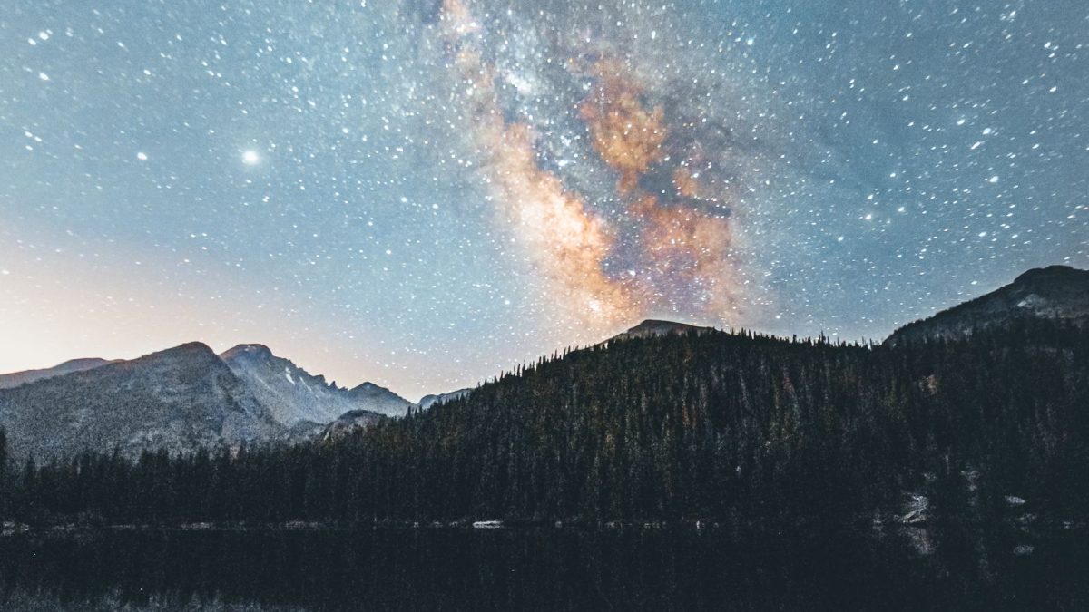 Milky Way stretching above a mountain lake and pine forest at night