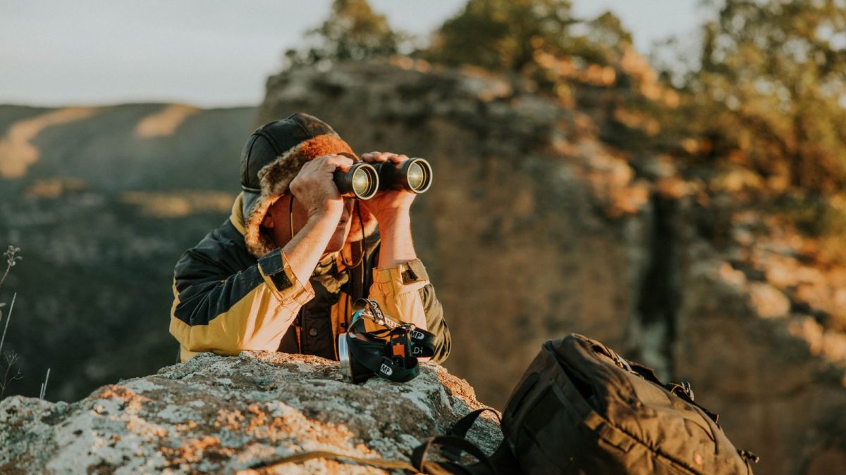 Hiker on a rocky overlook looking through binoculars at golden hour