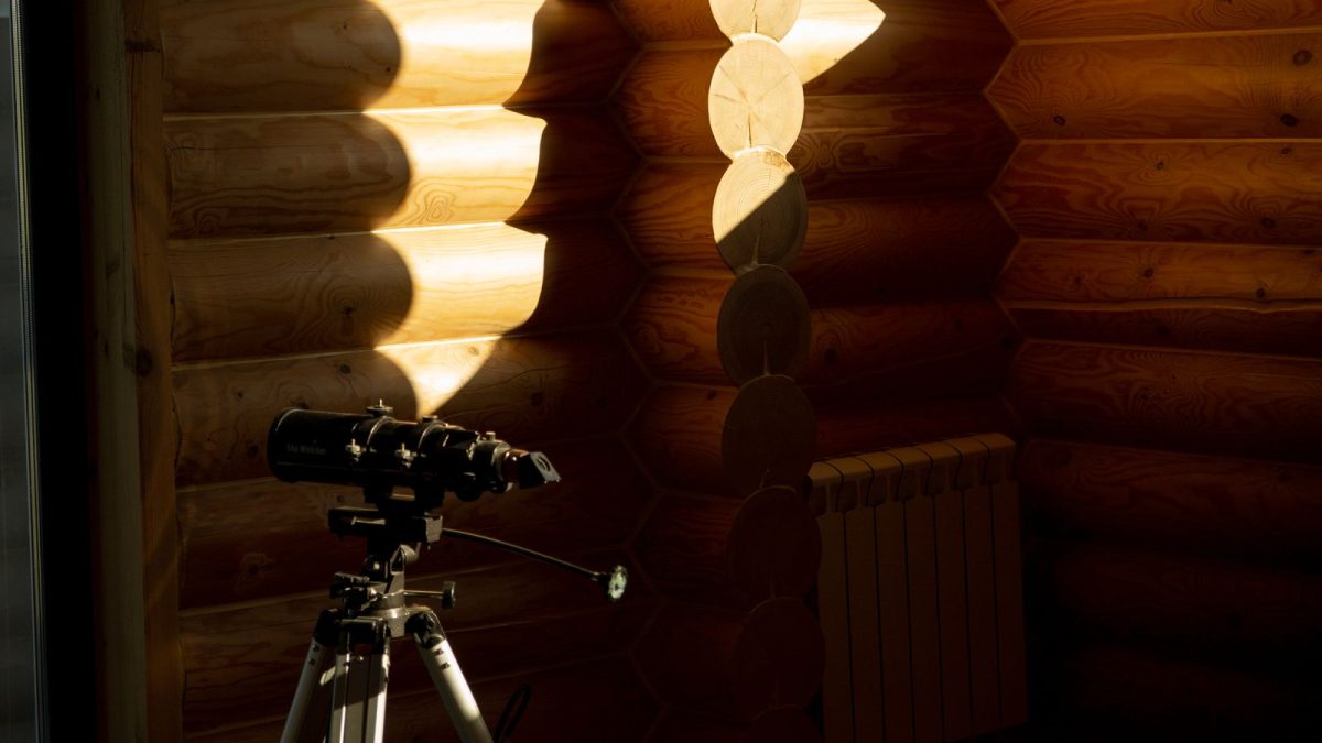 Telescope on a tripod beside a window in a log cabin